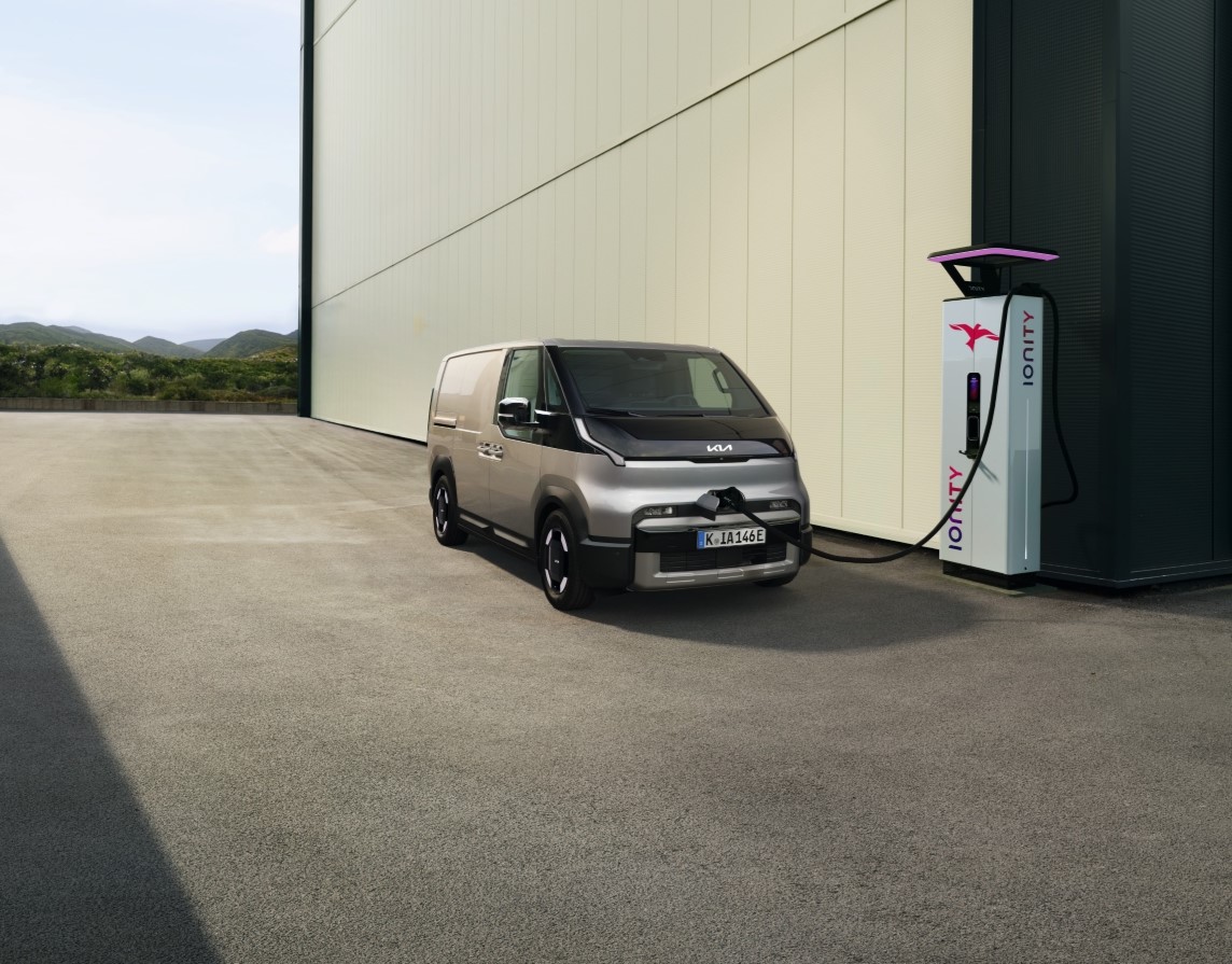 A PV5 Cargo charging at a charging station next a warehouse