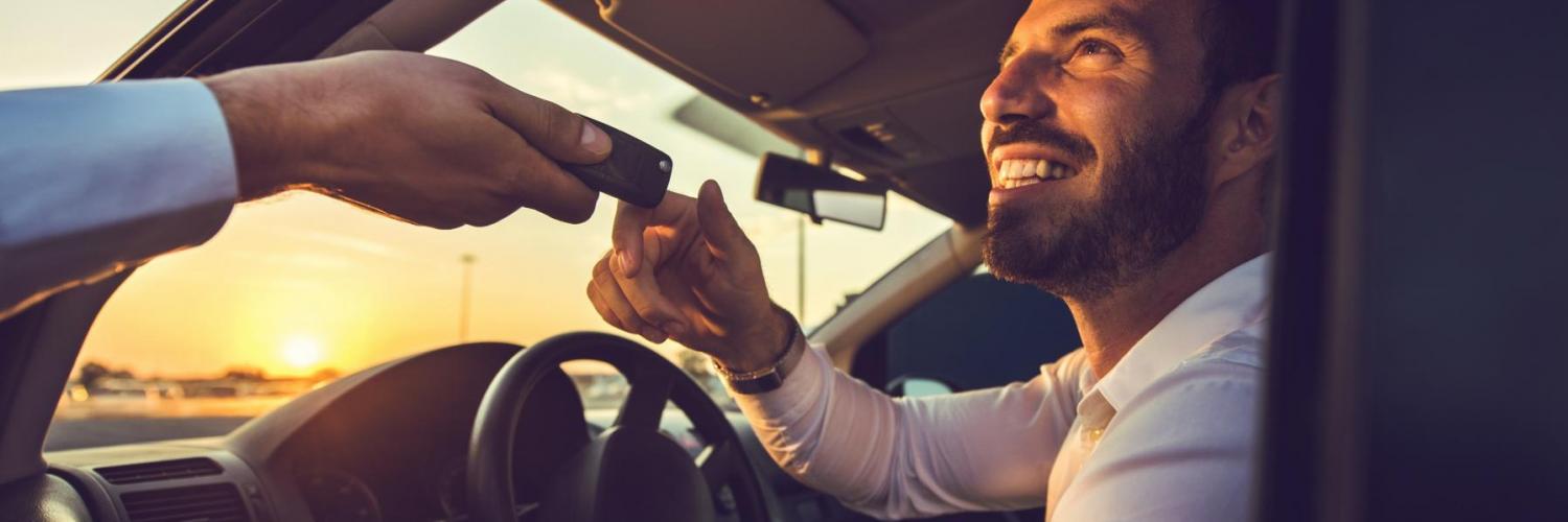 A man smiling behind the steering wheel receiving a car key