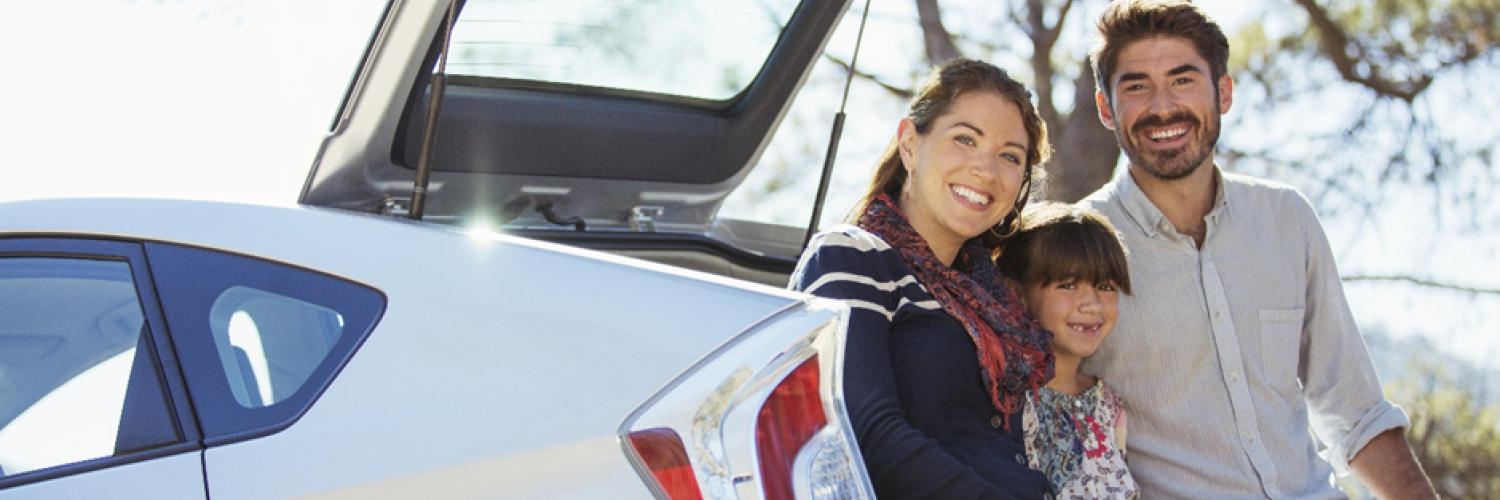 A family smiling at the back of their car A family smiling at the back of their car