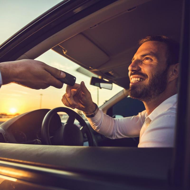 A man smiling behind the steering wheel receiving a car key