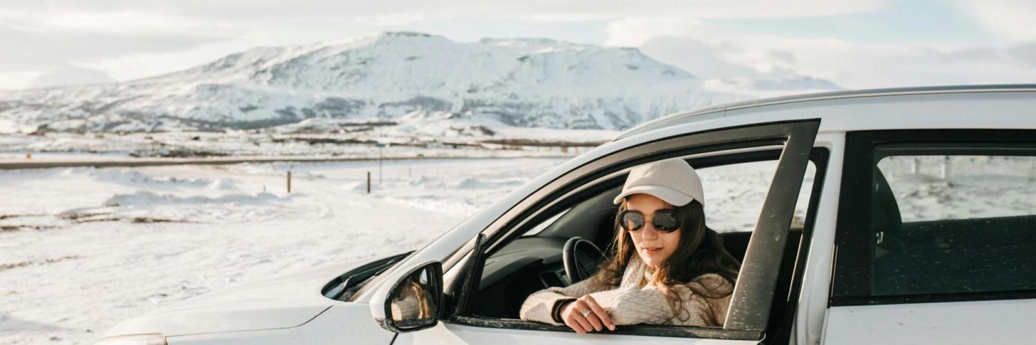 A woman sitting in a white car in a snowy landscape